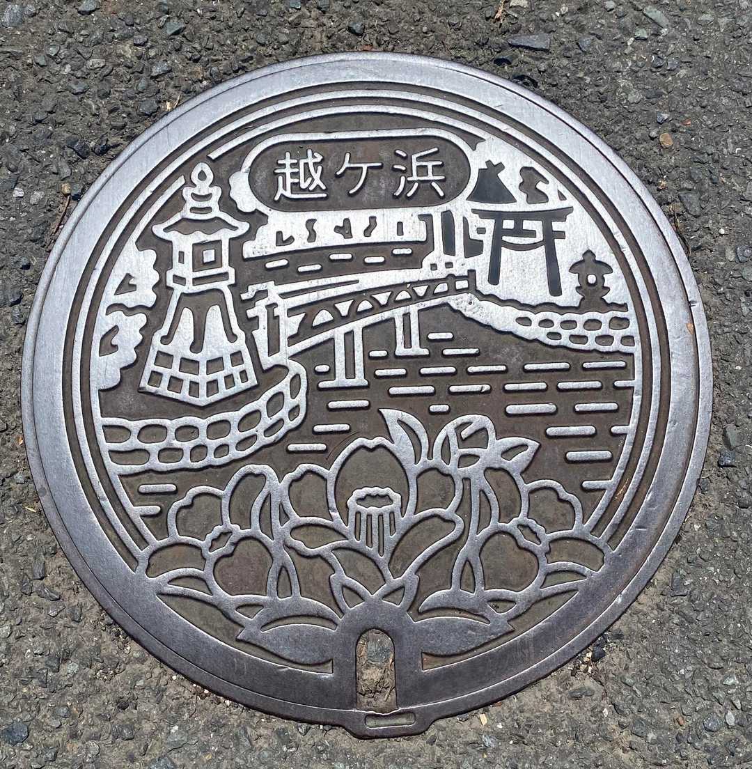 越ヶ浜のマンホール♪

越ケ浜地区は、笠山という火山と本土の間が砂礫の堆積で陸続きとなった場所に生まれた漁業集落です。
笠山は江戸時代から、景勝地として扱われており、虎ヶ崎にはヤブ椿が自生する椿群生林があります。
椿の花は、萩市内の地名に「椿」「椿東(ちんとう)」「椿西(ちんぜい)」という形で残っていることからも、所縁の深い花といえます。
また、明神池は地下から海水が出入りするため、潮の干満が見られ、周囲は玄武岩の溶岩が積み重なり、中から冷気が漏れだす「風穴」があります。