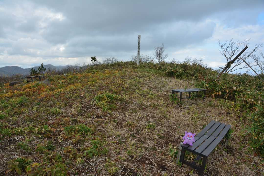 しかるのちに、今回の目的地である『ぼんてん山』の頂へ到着だ。山頂周辺は広場状に刈り払われており、ベンチなども設置されている。
ところで、写真中央付近に見える標柱には、「ぼんてん山登山道開通記念」「六ヶ所村山岳会 平成30年8月11日」と記されており、本峰への山路が拓かれたのはごく最近であることが伺える。すなわち、ここまで歩いてきた登山道は地元の山岳会有志の方々による整備の恩恵であり、大変頭の下がる思いであった。