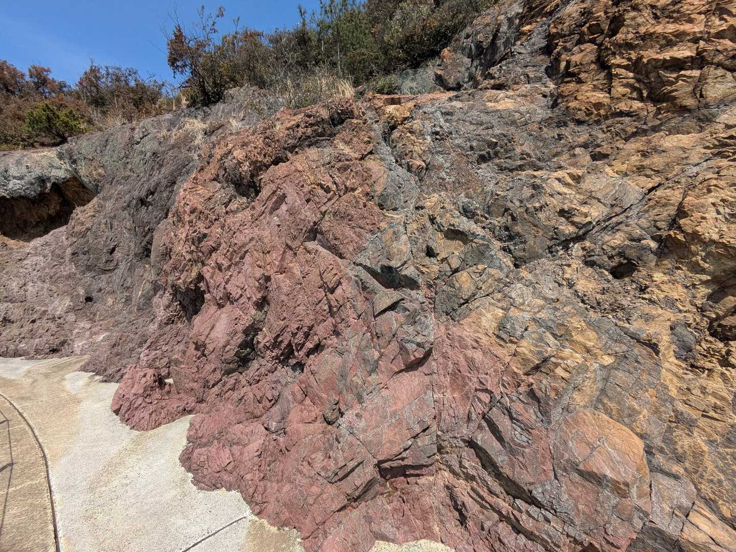 青・赤・黄・白・黒の5色に色づいた岩が連なる海岸の地層