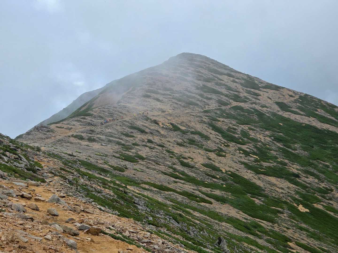 東天井岳から降りてきて。
向かう先は…
今、この写真をみて、あれが横通岳だったようです。
先行パーティー、私、後続パーティー、いずれもピークには向かわず、少し下がった(右下の)トラバース気味の道を進みました。
まあ、疲れてもきてますし、雲行きも怪しいので、これで良かったかなと思います。

後で知りましたが、登山道を進むと、ピークに登らず横を素通りしてしまうので横通岳というらしい。ほんと？😆