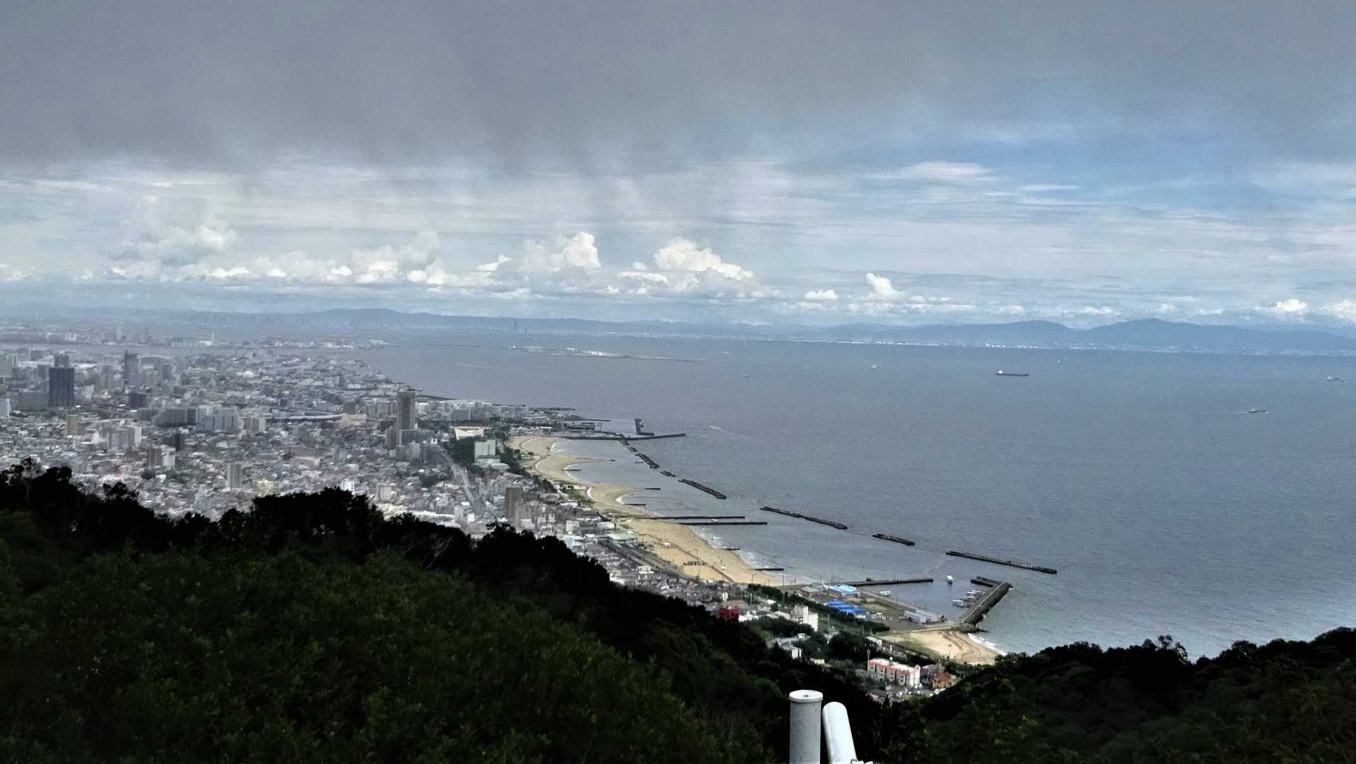 旗振山山頂から大阪湾方面を見る。大阪は日射しがあり、山々が見えている。六甲山上はやや暗い雲