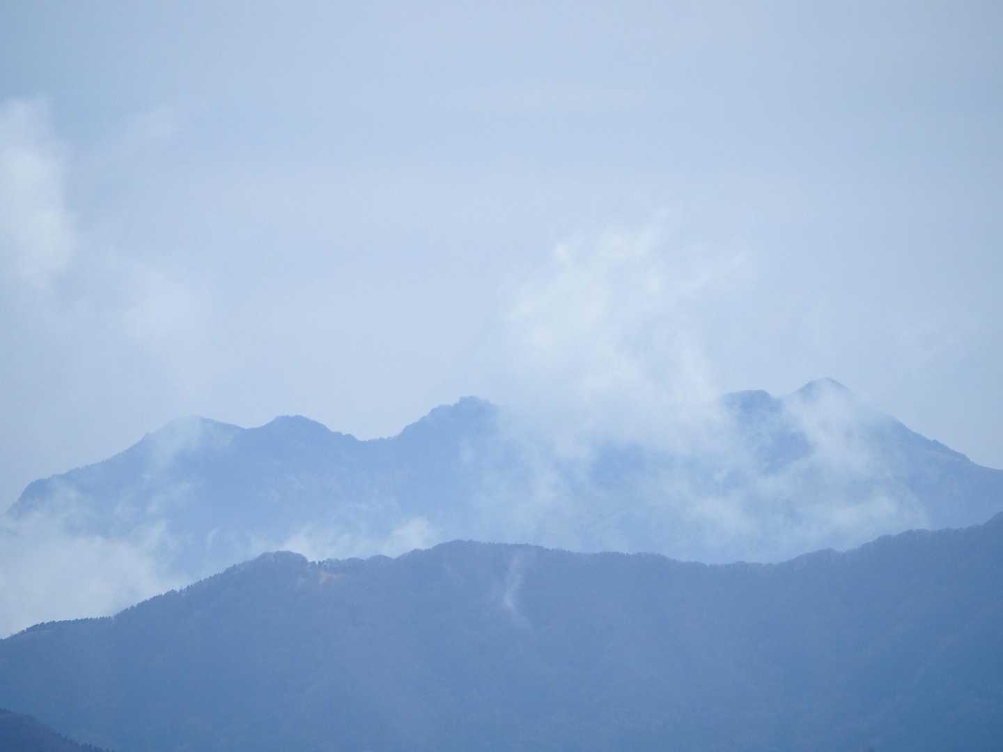 山頂の手前の木の切れ間から石鎚方面。雲の中に石鎚の峰が姿を現した。