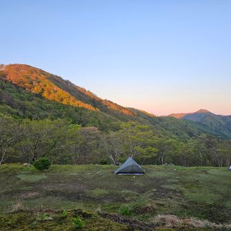 前山や薊岳が朝日に輝きます。
ところでこのテントが並んでいる平坦地、国土地理院の電子地図を見ると建物がありますが、実際にはその跡地です（地理院仕事しろ）。地図では横に長い大きな建物なので、何だったのか気になります。