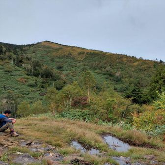 木道や沢のように雨水が流れる石ころだらけの登山道を慎重に登る
なかなか下の芝に到着しないので、少し手前で乾いた石を探し休憩
右側にリフト乗り場が見える