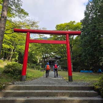 鳥居に合わせたように真っ赤なザックを背負う仲間が、登山口である公時山神社を参拝し、安全登山を祈願する。