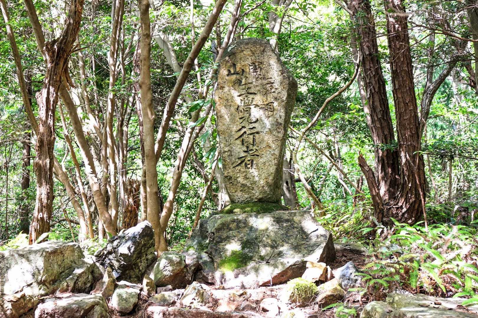 　先ほどの三差路からさらに200mほど進むと、登山道の左側にこのような石碑が建てられいた。

　…この石碑には「開山 二代目 ◯覚行者」と彫られていたが、◯の文字がはっきりしないものの、「生・主・王」の何れかなので、この人物を検索したが、ヒットしなかった。
　御嶽山の大衆信仰を広めた覚明行者と普寛行者は、日進市の御岳山や松平の岩谷山を調べた時にヒットしたが、何れにしても「覚」の文字を継承しているため、この二人の行者の流れを汲む人物と考えられた…。